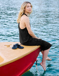 Woman sitting on a red and yellow boat in water wearing a black racerback dress.
