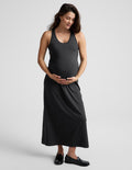 Pregnant woman wearing a black racerback dress against a plain background.