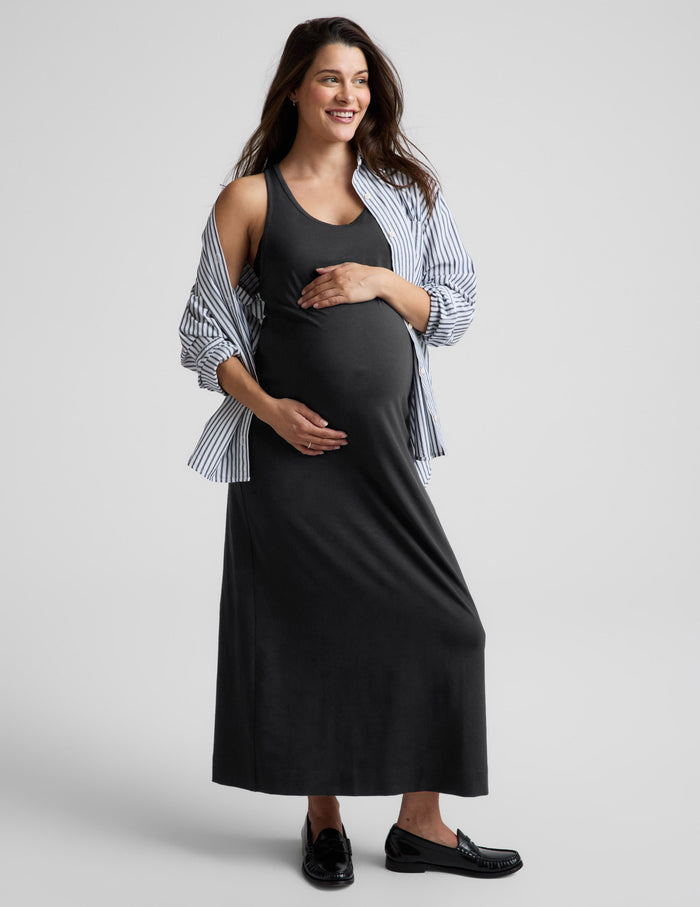 Pregnant woman wearing a black racerback dress against a plain background.