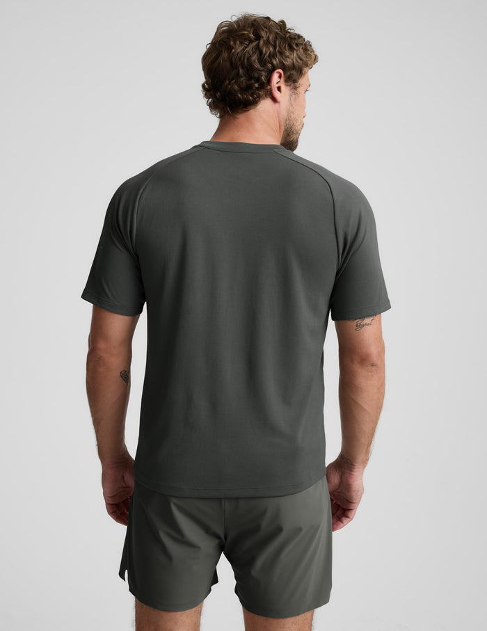 Man wearing a dark green t-shirt and shorts on a light gray background.
