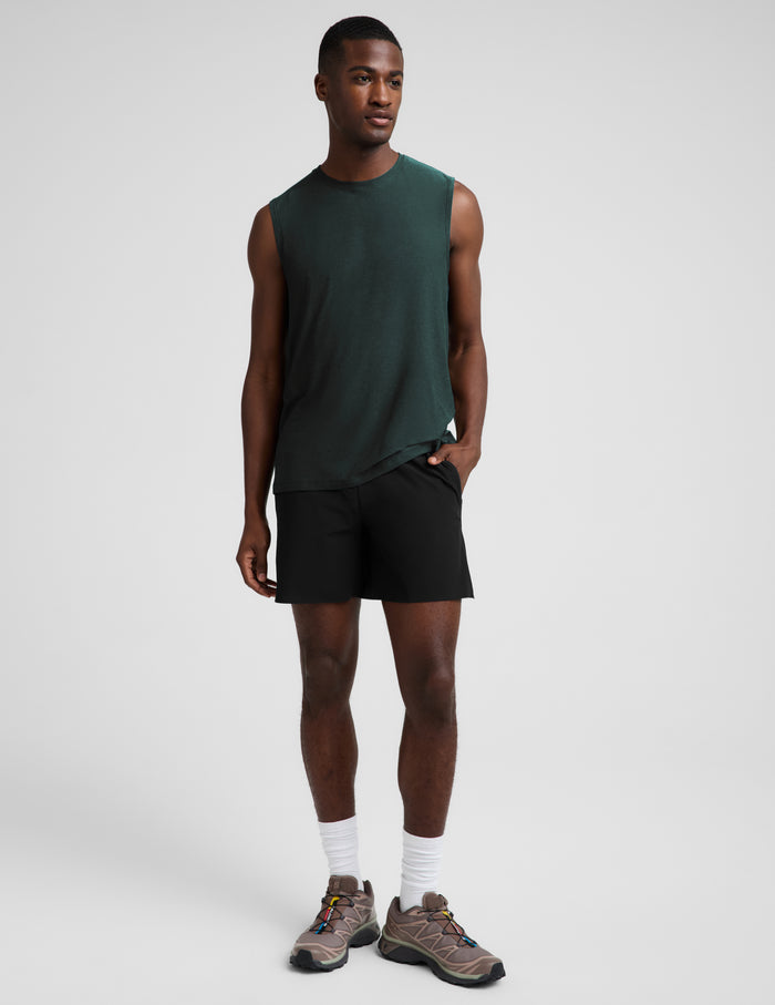 Man wearing a dark green muscle tank top and black shorts against a plain studio background.