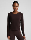 A woman modeling a dark brown long-sleeve crewneck top and matching dark brown leggings against a light gray studio background.