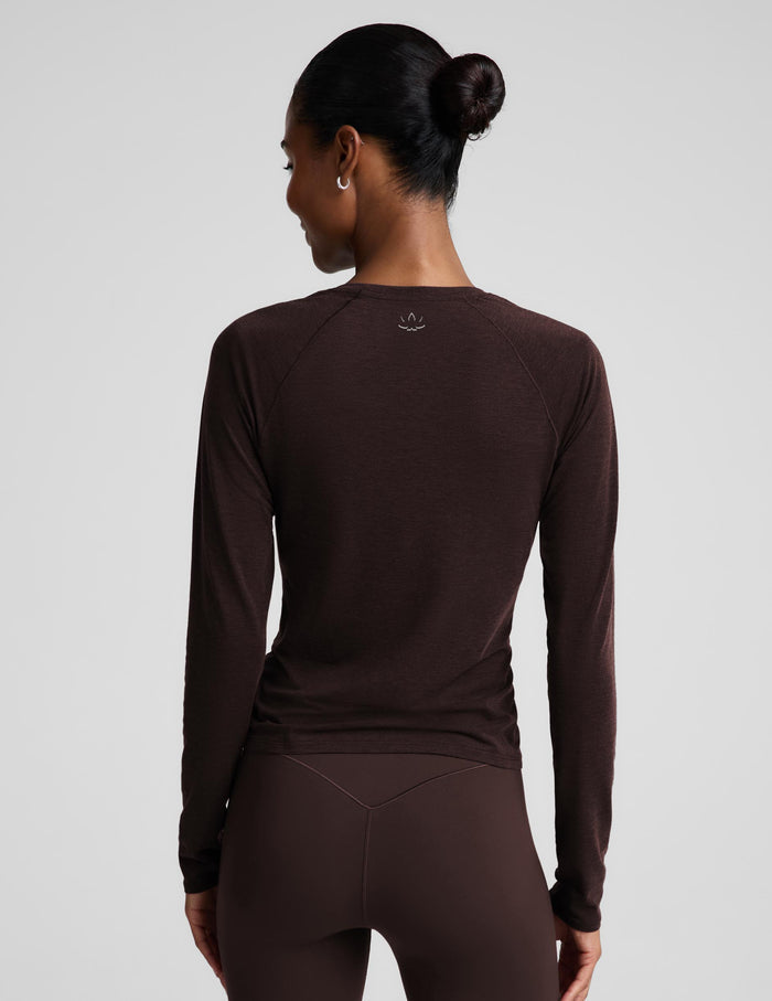 A woman modeling a dark brown long-sleeve crewneck top and matching dark brown leggings against a light gray studio background.