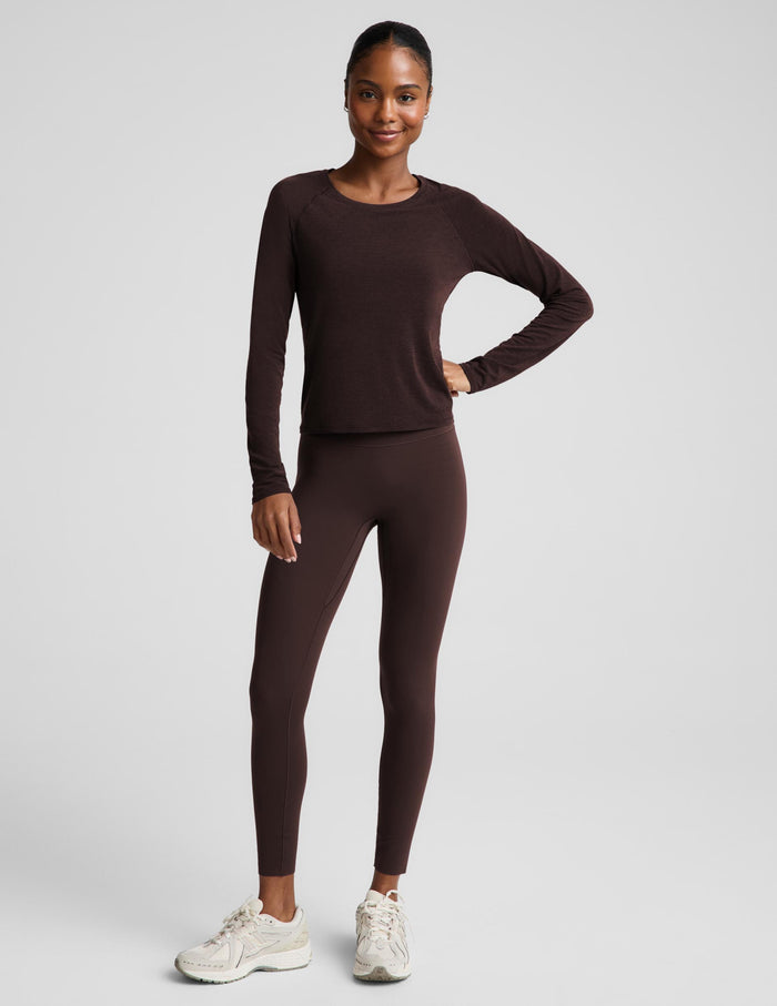 A woman modeling a dark brown long-sleeve crewneck top and matching dark brown leggings against a light gray studio background.