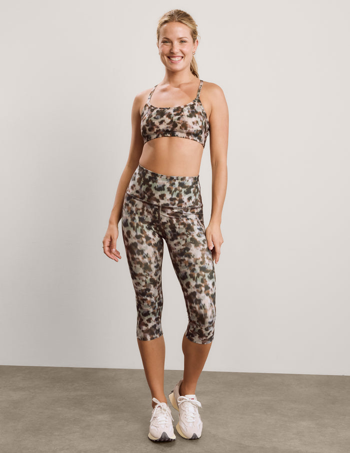 Woman wearing a printed sports bra and capri leggings against a plain background.