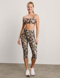 Woman wearing a printed sports bra and capri leggings against a plain background.