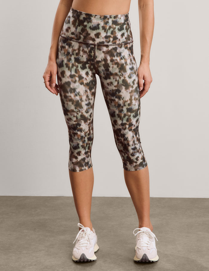Woman wearing a printed sports bra and capri leggings against a plain background.