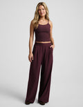 A woman modeling a matching two-piece set consisting of a dark burgundy tank top and wide-leg pants, photographed against a light gray studio background.