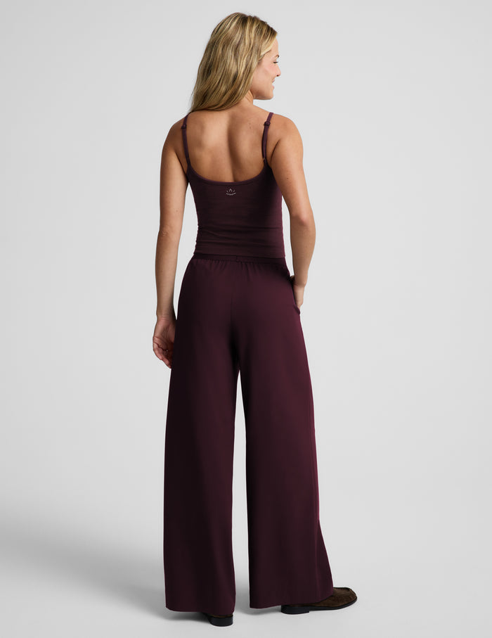A woman shown from the back wearing a tank top and wide leg pants in deep burgundy, photographed against a light gray studio background.