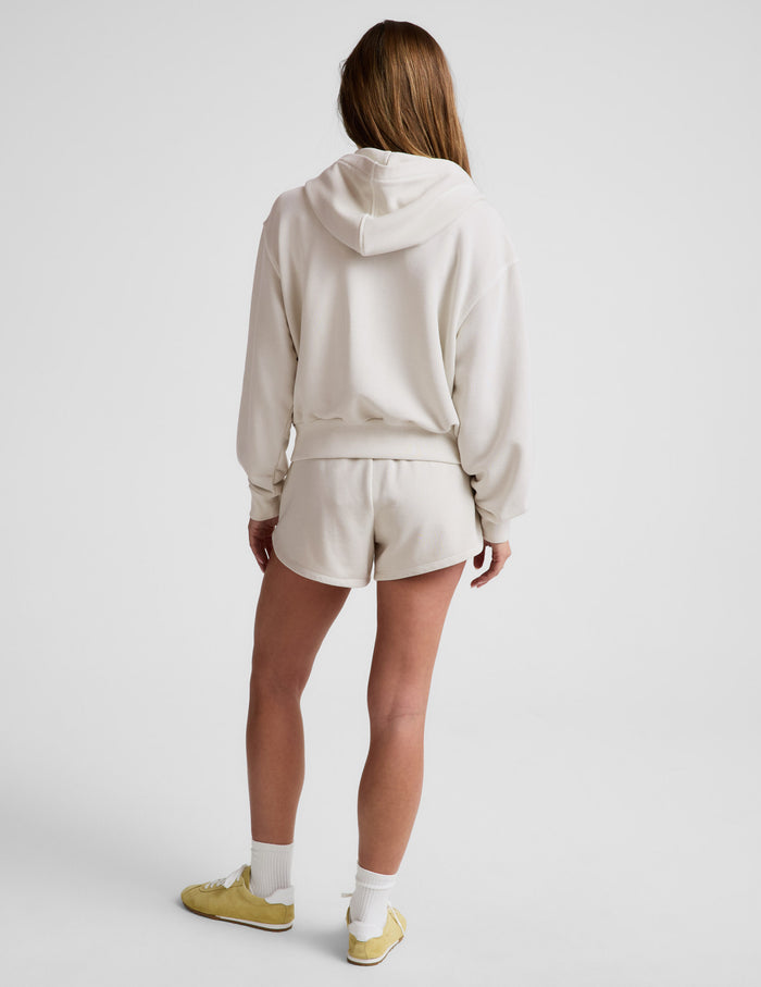 Woman wearing a white sweatshirt and shorts on a plain background.