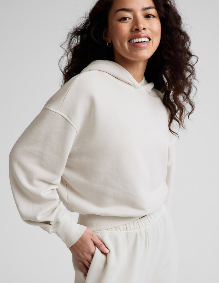 Woman wearing a white hoodie and pants against a plain background.