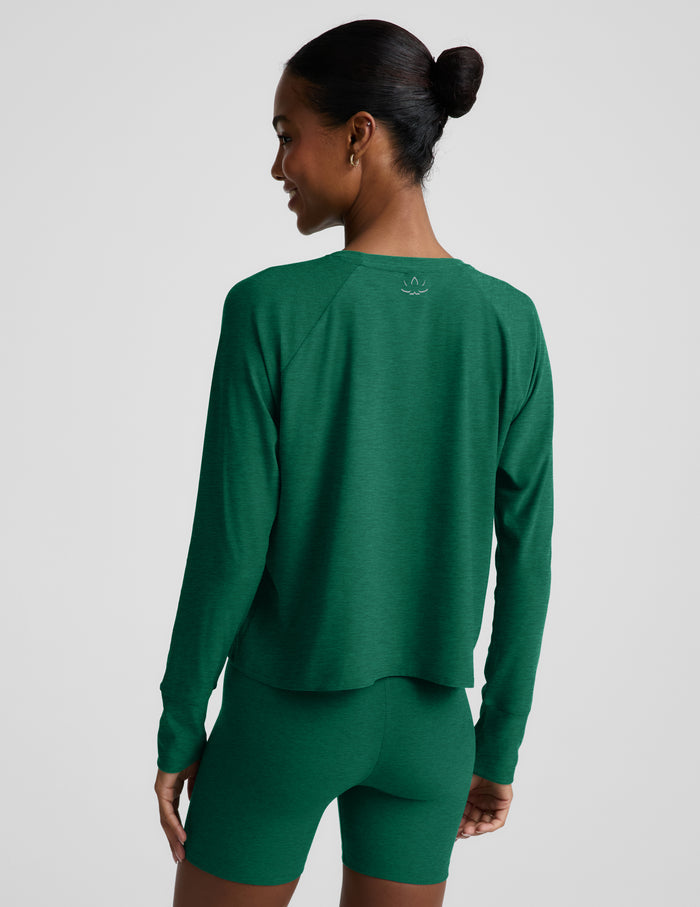 Woman wearing a green long sleeve top and biker shorts against a plain background.