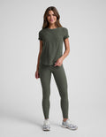 Woman wearing a green t-shirt and leggings set on a light gray background.