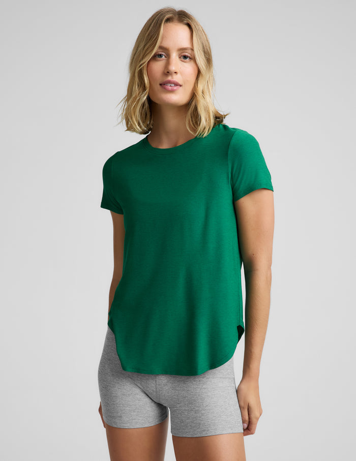 Woman wearing a green short sleeve t-shirt and gray 3" biker shorts against a plain background.