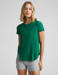 Woman wearing a green short sleeve t-shirt and gray 3" biker shorts against a plain background.