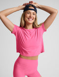 Woman wearing a pink cropped short sleeve top and biker shorts against a plain background.