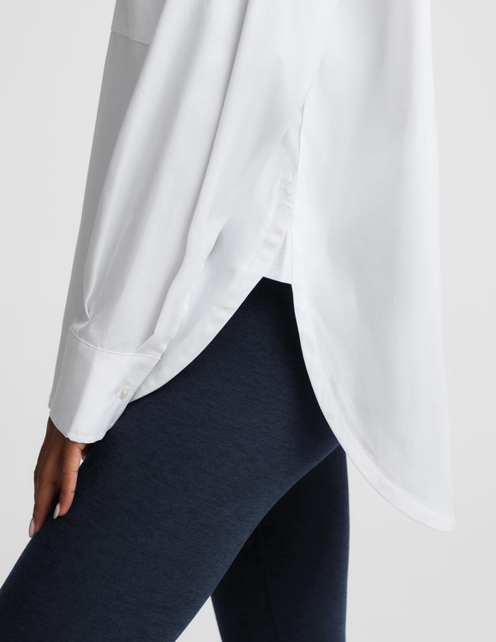 A close-up of a person wearing a loose white long-sleeve blouse and dark navy leggings against a light gray studio background.