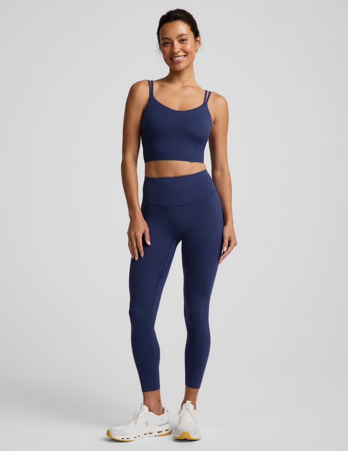 Woman wearing a blue cropped tank and blue midi leggings against a plain background.