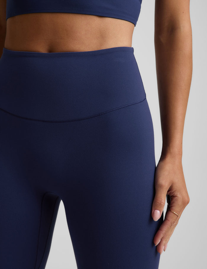 Woman wearing a blue cropped tank and blue midi leggings against a plain background.