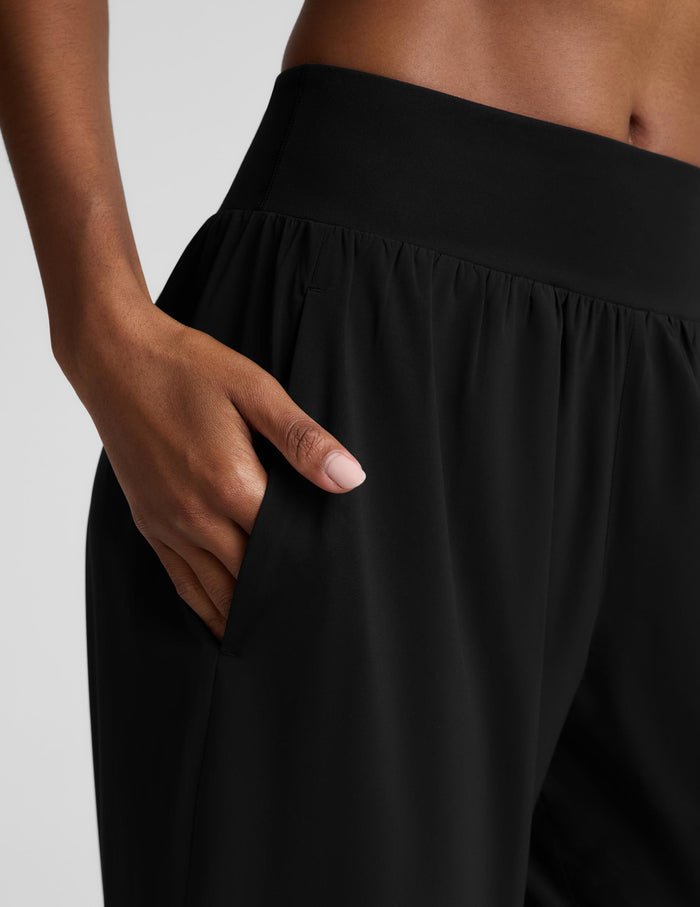 A woman modeling a black two-piece activewear set consisting of a cropped tank top and high-waisted wide-leg pants, photographed against a solid light gray studio background.