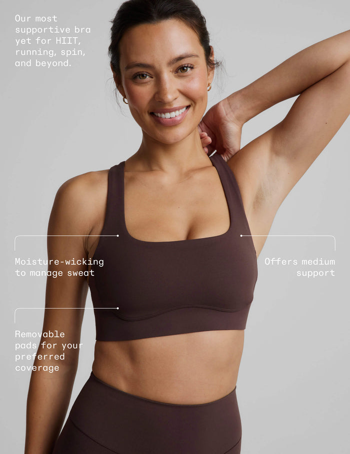 Woman wearing a brown sports bra and brown biker shorts against a plain background.