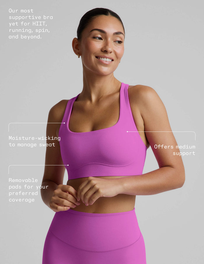 Woman wearing a purple sports bra and purple midi length leggings against a plain studio background.