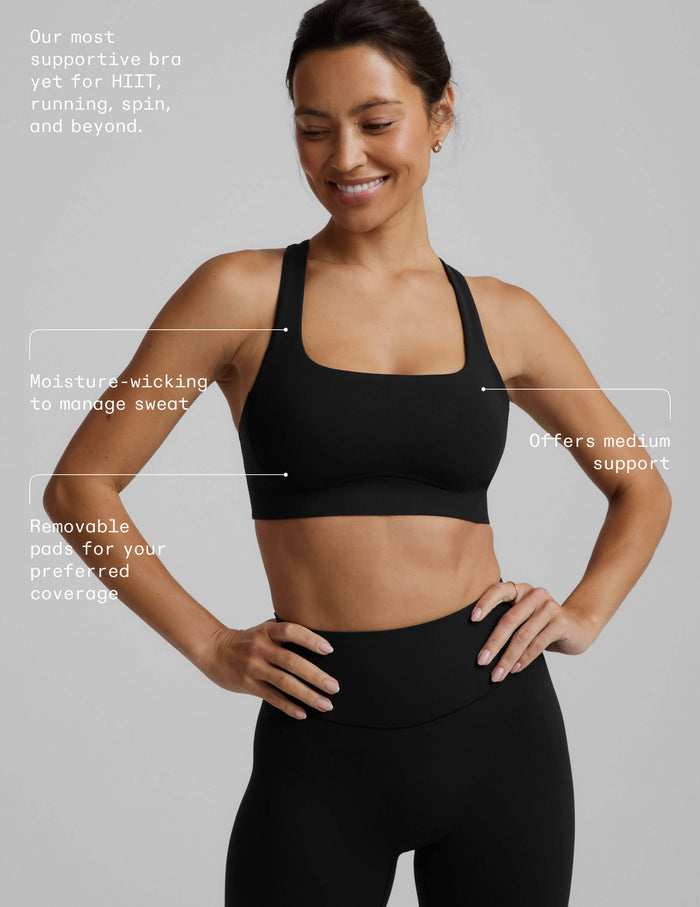 A woman in a black sports bra and black midi length leggings against a plain background with text product callouts on top.