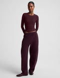 A model wearing a matching dark burgundy two-piece lounge set consisting of a long-sleeve top and wide-leg sweatpants, photographed against a neutral light gray studio background.