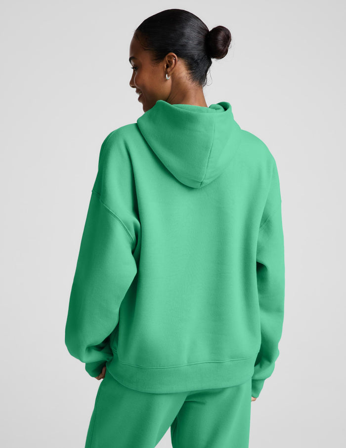 A woman wearing a bright green pullover hoodie and matching sweatpants, photographed against a plain light gray studio background.