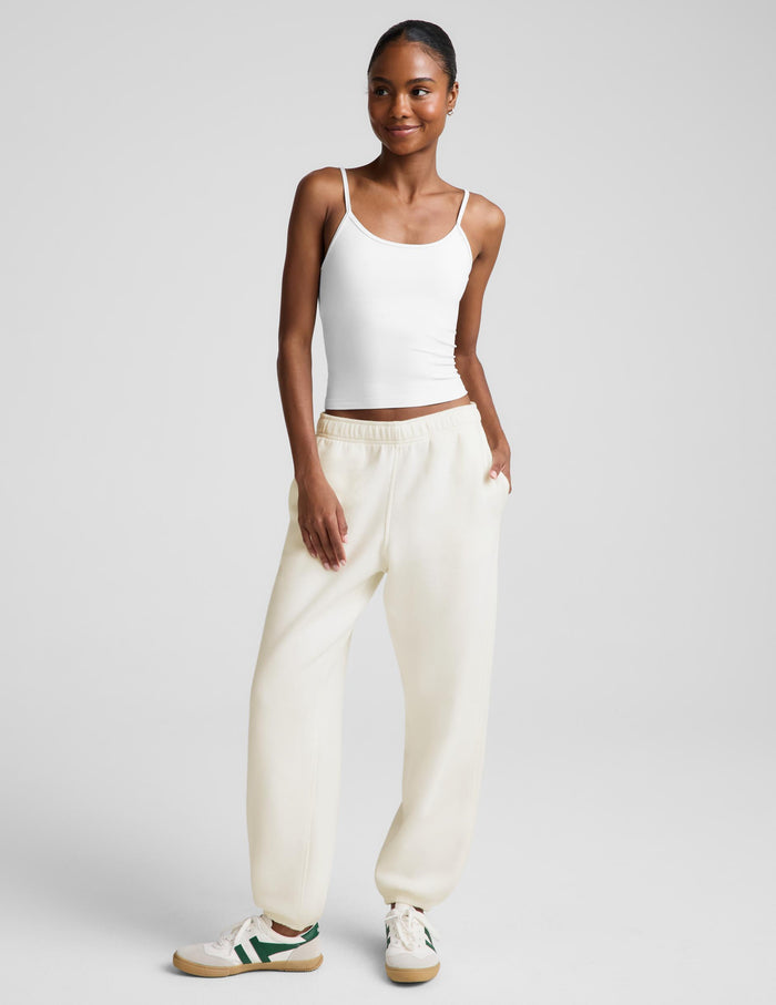 A model wearing a white camisole top and cream-colored wide-leg sweatpants, paired with white sneakers, against a light gray studio background.