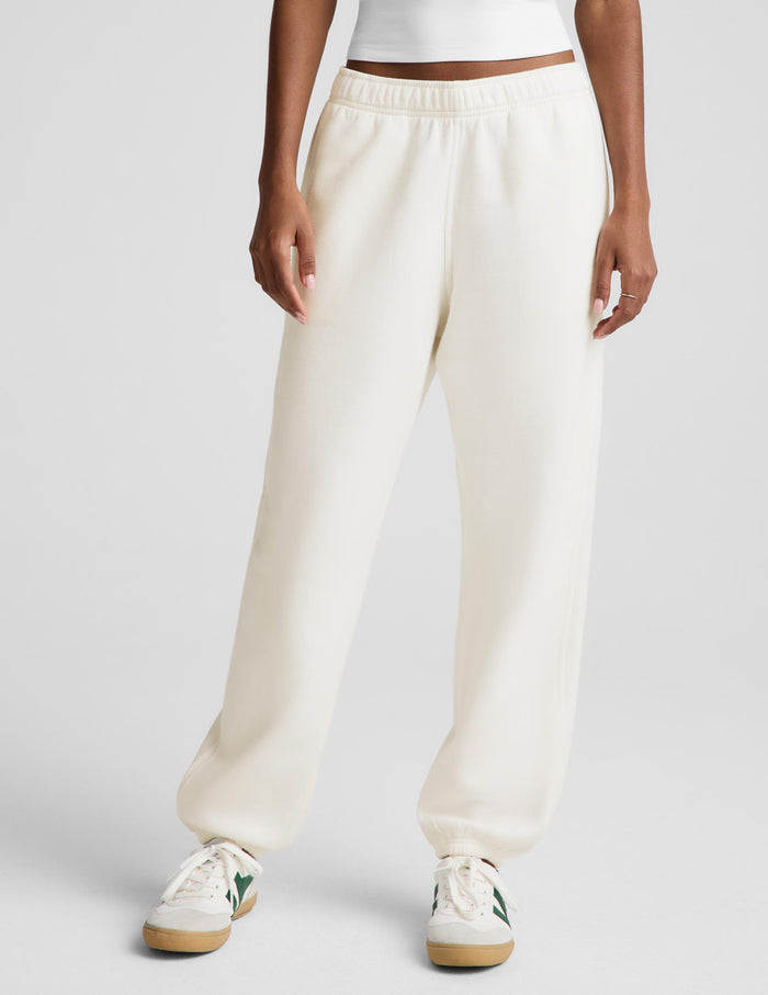 A model wearing a white camisole top and cream-colored wide-leg sweatpants, paired with white sneakers, against a light gray studio background.