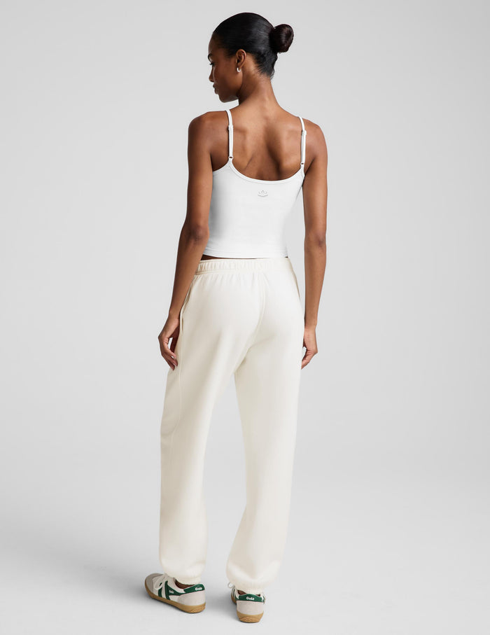 A model wearing a white camisole top and cream-colored wide-leg sweatpants, paired with white sneakers, against a light gray studio background.