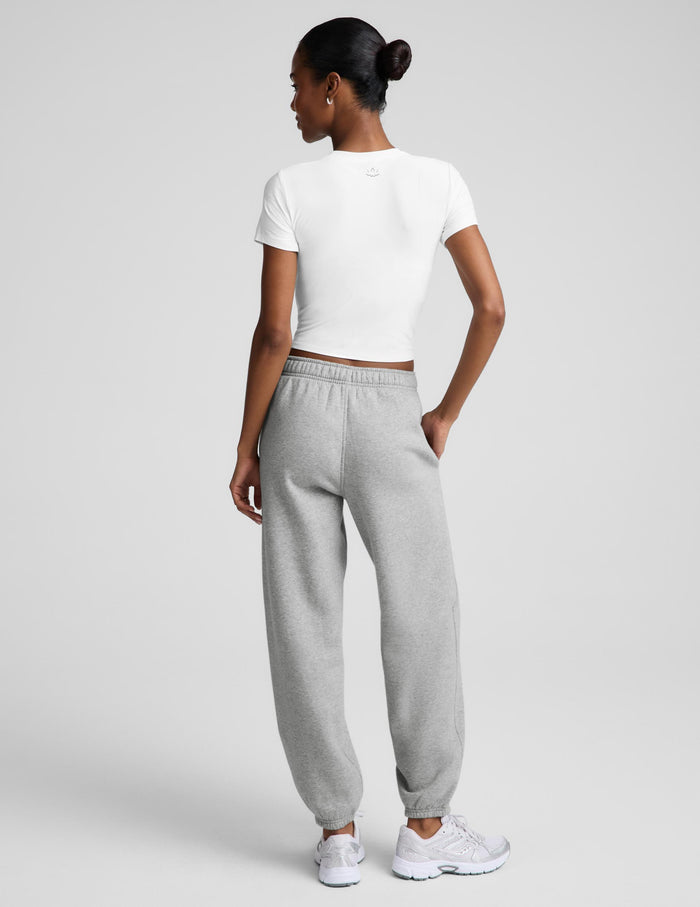 A woman shown from the back wearing a white short-sleeve crop top and light gray jogger sweatpants, paired with white sneakers, against a light gray studio background.