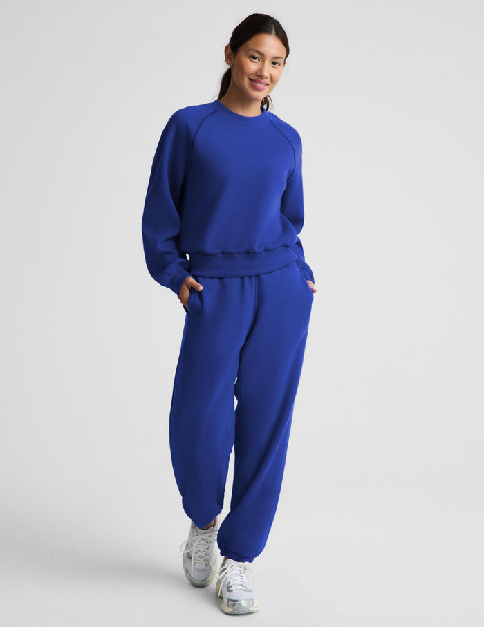 A woman modeling a matching royal blue sweatshirt and jogger pants set against a light gray studio background.
