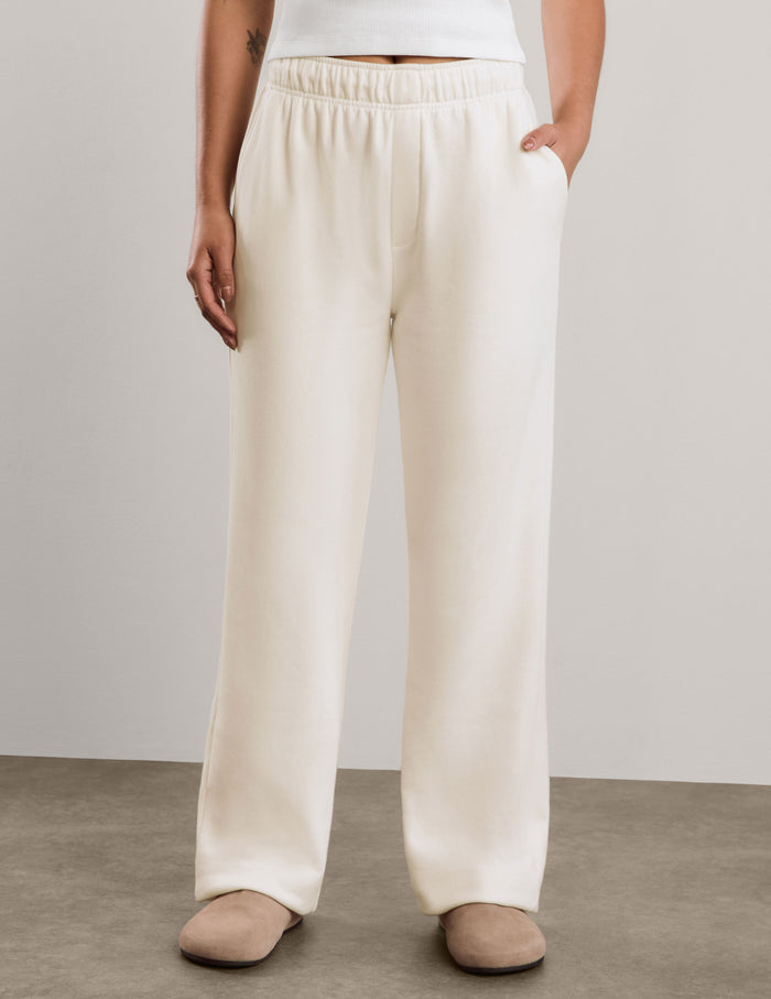 A woman modeling a white short-sleeve cropped top and off-white wide-leg sweatpants against a neutral studio backdrop.