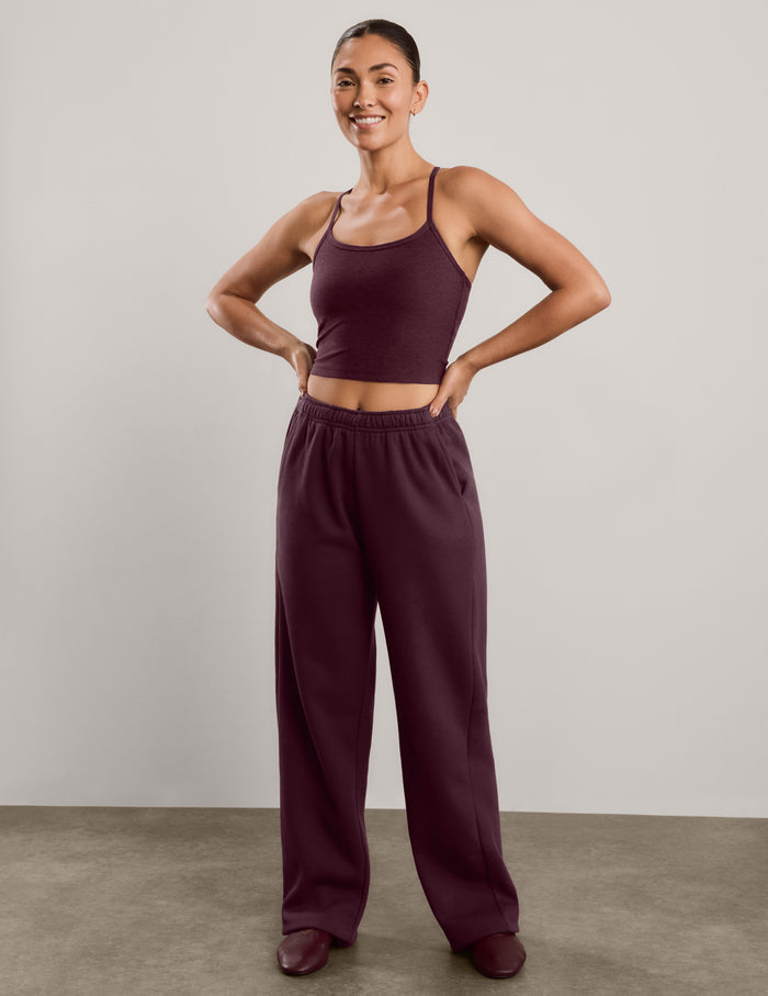 A woman modeling a matching two-piece lounge set consisting of a dark burgundy camisole top and matching wide-leg sweatpants, standing against a neutral studio background.