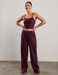 A woman modeling a matching two-piece lounge set consisting of a dark burgundy camisole top and matching wide-leg sweatpants, standing against a neutral studio background.