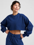 Woman wearing a blue sweatshirt and sweatpants on a plain background.