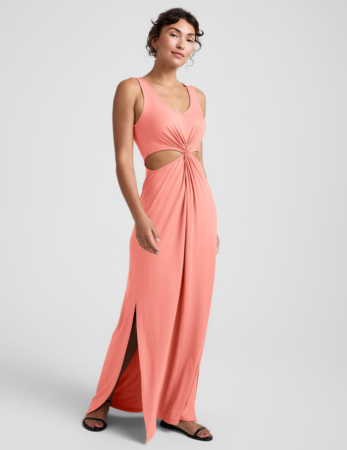 Woman wearing a coral pink maxi dress with cut-out design on a light gray background.