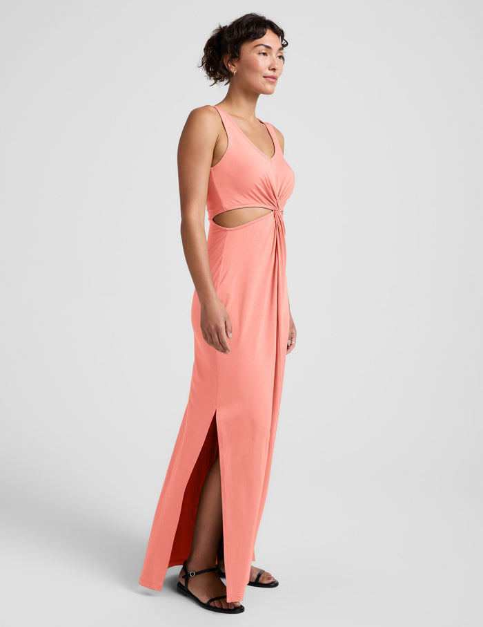 Woman wearing a coral pink maxi dress with cut-out design on a light gray background.