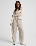 A woman modeling a matching beige set consisting of a cardigan and barrel leg drawstring pants, paired with white sneakers, against a light gray studio background.