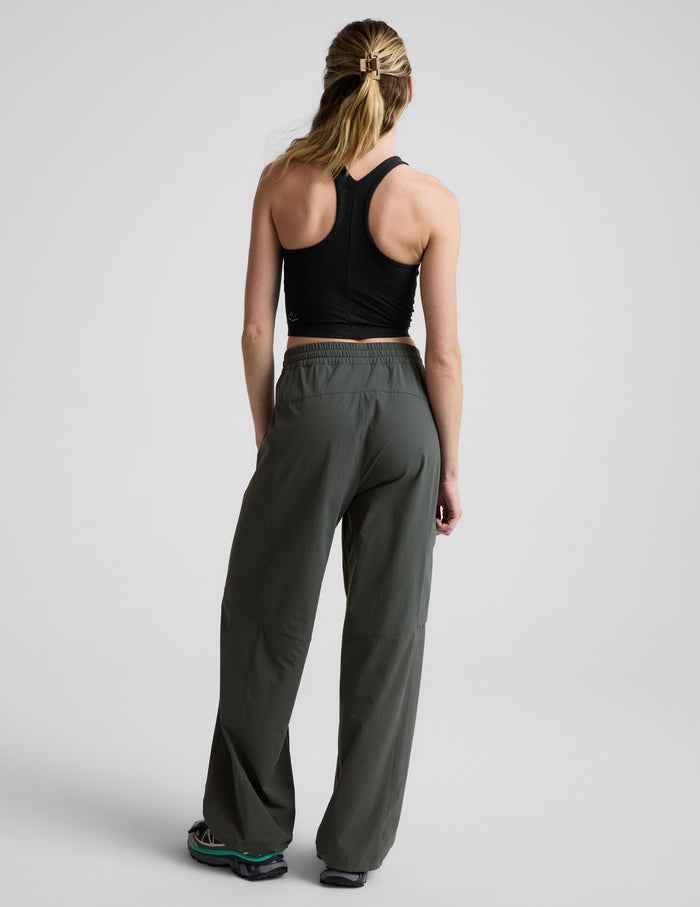 Rear view of woman wearing dark olive Peak Pant™ with a gathered waistband, paired with a black racerback tank top.