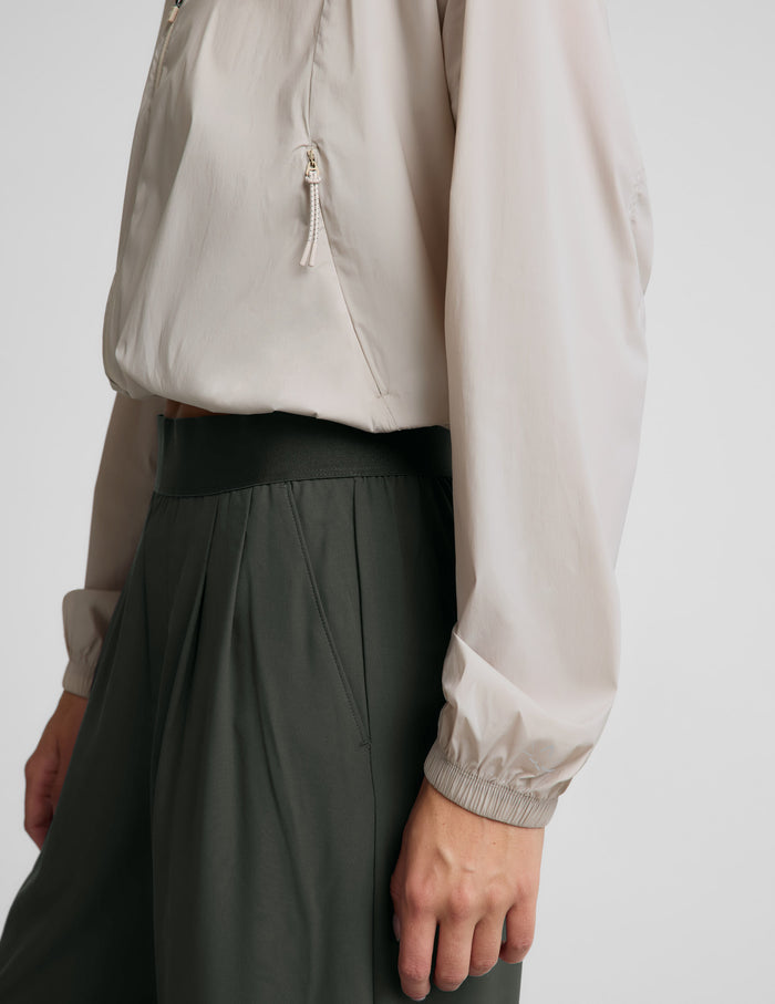 Woman wearing a beige jacket and green pants against a plain background.