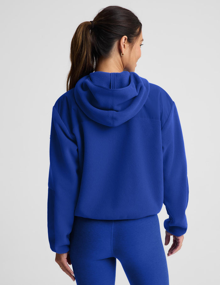 A woman shown from the back wearing a bright royal blue cropped hoodie and matching blue leggings against a light gray studio background.