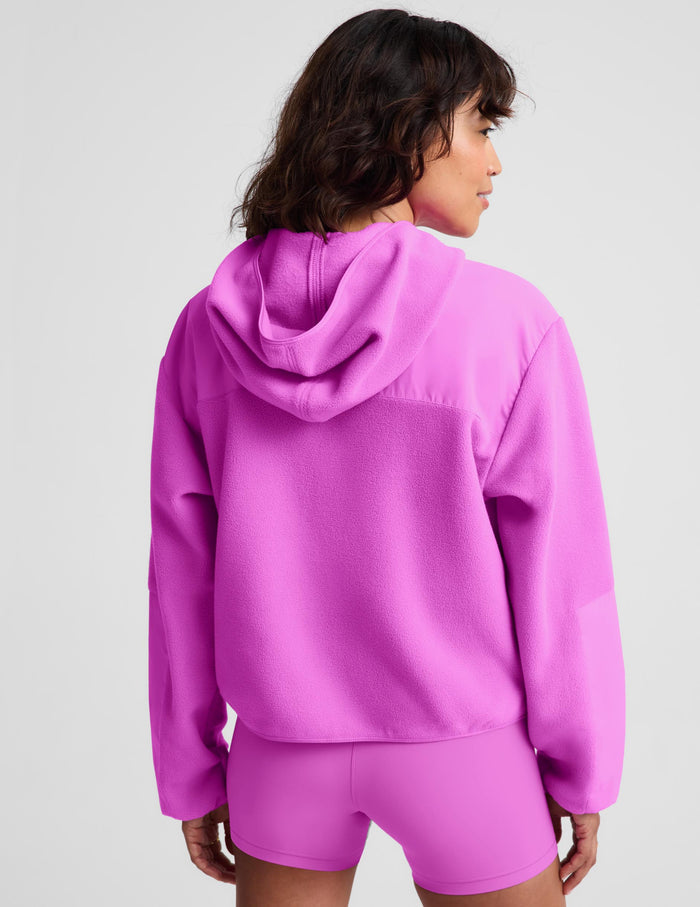 A woman shown from the back wearing a bright pink cropped hoodie and matching fitted shorts against a light gray studio background.