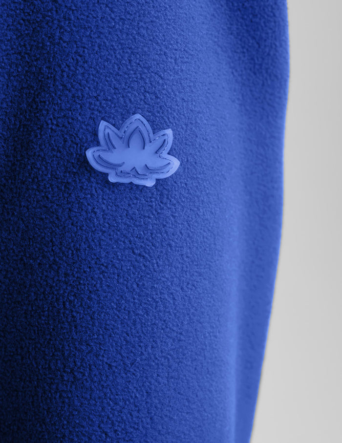 A close-up of a textured royal blue fleece garment featuring a small, tonal light blue embroidered lotus flower logo.
