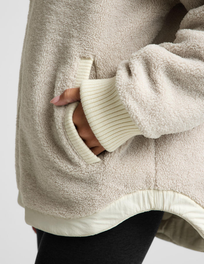 A woman modeling a cream-colored quilted zip-up jacket, paired with black leggings and silver sneakers, against a light gray studio background.