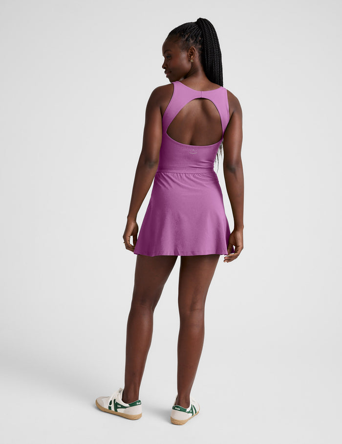 Woman wearing a purple mini dress with built-in pocket shorts against a plain background.