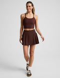 Woman wearing Brown Score™ Pleated Skirt with stitch down front pleats, paired with a matching cropped tank and sneakers.