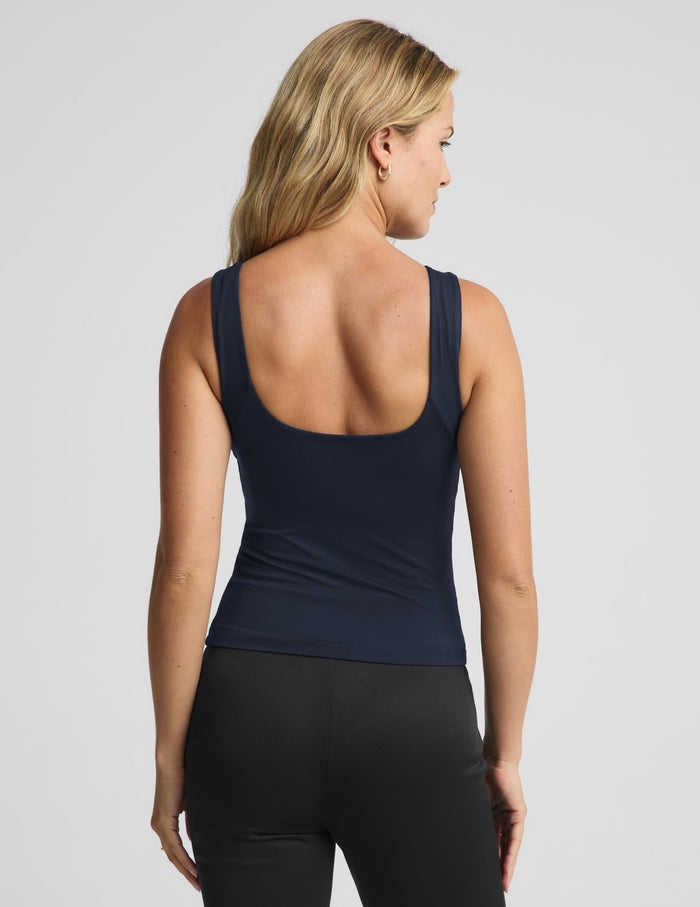 A woman shown from the back wearing a navy blue scoop-neck tank top and black leggings against a light gray studio background.